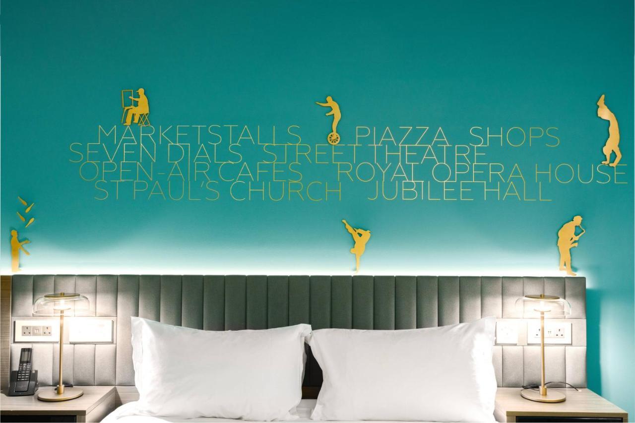 Middle Eight - Covent Garden - Preferred Hotels And Resorts London Ngoại thất bức ảnh The photo shows a modern hotel room with a distinctive turquoise wall. On the wall, there are gold silhouettes of people engaged in various activities, suggesting movement or leisure. The wall also features text that highlights local attractions like