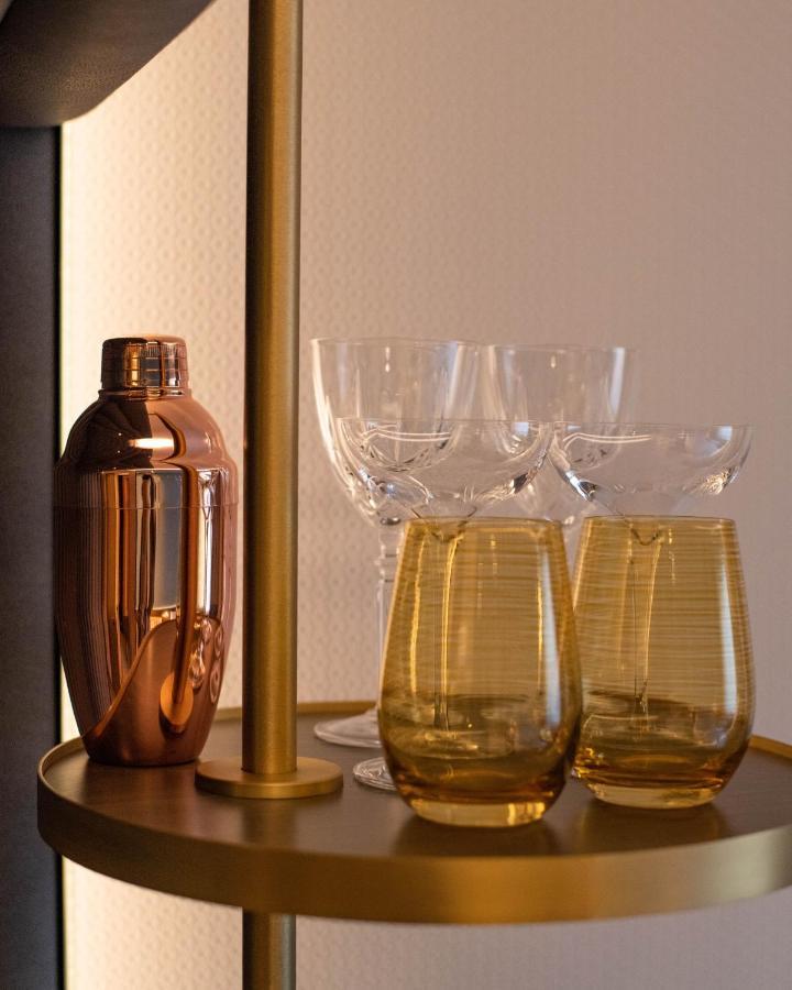 Middle Eight - Covent Garden - Preferred Hotels And Resorts London Ngoại thất bức ảnh The photo shows a stylish bar setup featuring a shiny copper cocktail shaker positioned next to several elegant glassware pieces. There are four tall, clear stemmed glasses and two round, amber-colored glasses with a textured pattern. The background 