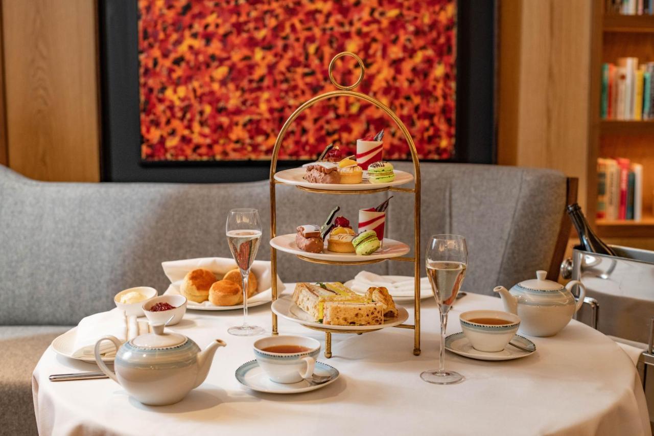 Middle Eight - Covent Garden - Preferred Hotels And Resorts London Ngoại thất bức ảnh The photo shows an elegant afternoon tea setup on a white tablecloth. At the center, there is a multi-tiered stand displaying a variety of pastries and desserts, including cakes and colorful sweets. Surrounding the stand are teapots and teacups, read