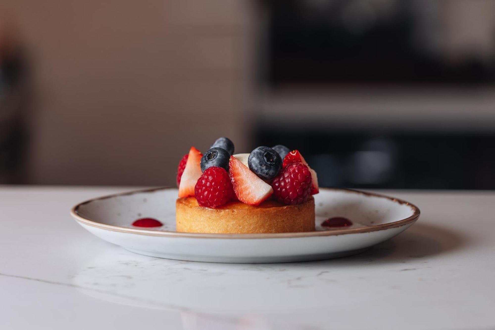 Middle Eight - Covent Garden - Preferred Hotels And Resorts London Ngoại thất bức ảnh The photo shows a delicious-looking dessert on a white plate. The dessert appears to be a small tart or cake topped with fresh strawberries, raspberries, and blueberries. It has a golden crust, and there are small dollops of a red sauce or fruit pure